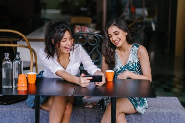 İki yakın arkadaş (kadınlar) gün boyunca bir kafede oturup bir video birlikte Smartphone'da izlerim. Video ve birbirlerinin şirket zevk olarak her ikisi de gülüyorsun.