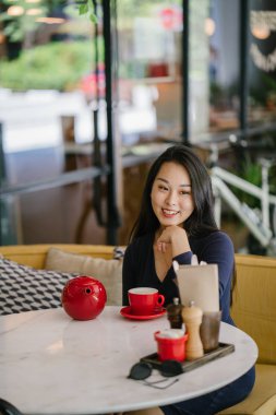 Bir açık havada açık havada oturan ve kırmızı bir çay seti çay sıcak bir fincan zevk genç, çekici, zarif ve güzel Asyalı kadın Portresi. 