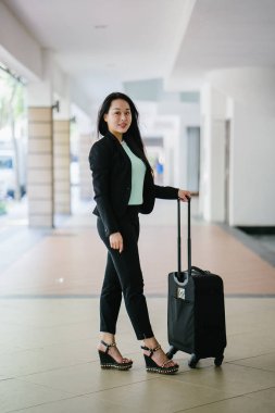 Genç bir Asyalı kadın bavulunu çekiyor. O çekici, zarif ve şık giyinmiş