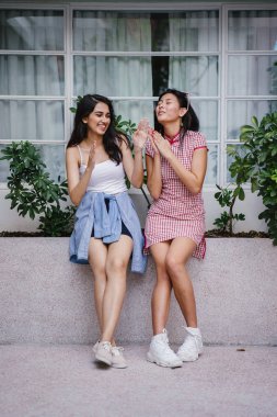 farklı etnik yapı birlikte dışarı asılı iki genç kadın arkadaşlar. Bir Çinli bir kadını bir cheongsam ve diğer bir Hint kadının modaya uygun bir kıyafet olduğunu