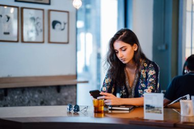 gün boyunca bir kafede kahve seviyor gibi genç Hintli Asya öğrenci kız onun smartphone denetliyor