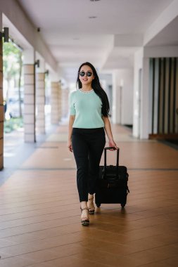 Genç bir Asyalı kadın bavulunu çekiyor. O çekici, zarif ve şık giyinmiş