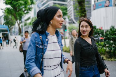 İki arkadaş, Orchard Road, Singapur, Asya 'da aydınlık bir yaz gününde mutlu bir şekilde yürüyüp konuşurlar. Biri Müslüman Malezyalı, diğeri Çinli bir kadın.. 