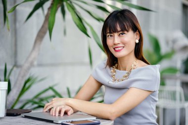 Açık havada şık bir yerde oturan bir emin, şık ve çekici orta yaşlı Çinli Asyalı kadın portresi. O bir pohpohlama gri kıyafeti giyiyor.