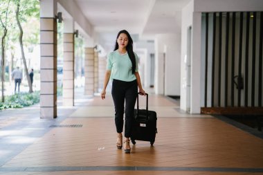 Genç bir Asyalı kadın bavulunu çekiyor. O çekici, zarif ve şık giyinmiş