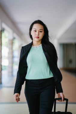 Genç bir Asyalı kadın bavulunu çekiyor. O çekici, zarif ve şık giyinmiş