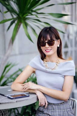 Açık havada şık bir yerde oturan bir emin, şık ve çekici orta yaşlı Çinli Asyalı kadın portresi. O bir pohpohlama gri kıyafeti giyiyor.