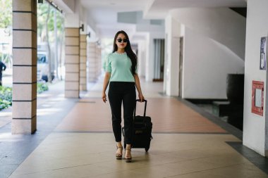 Genç bir Asyalı kadın bavulunu çekiyor. O çekici, zarif ve şık giyinmiş