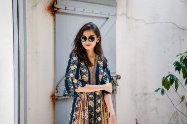 uzun boylu, zarif ve güzel Hint Asyalı kadın yaz elbise ve güneş gözlüğü gülümsüyor o pozlar gün boyunca bir arka sokakta bir sokakta olarak içinde