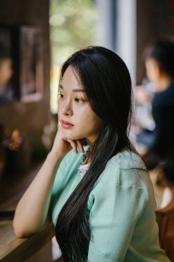 Genç ve çekici Çinli Asyalı bir kadının portresi uzanarak ve bir hafta sonu gün boyunca bir kafede rahatlatıcı. Nane yeşili bir kazak giyiyor.