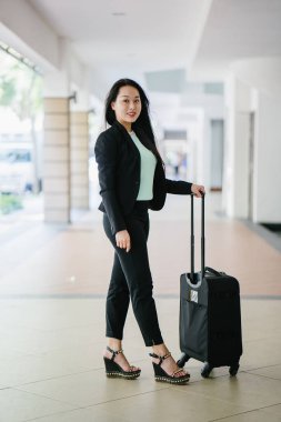 Genç bir Asyalı kadın bavulunu çekiyor. O çekici, zarif ve şık giyinmiş