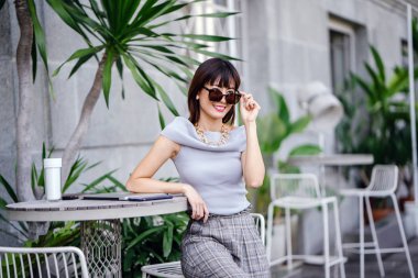 Açık havada şık bir yerde oturan bir emin, şık ve çekici orta yaşlı Çinli Asyalı kadın portresi. O bir pohpohlama gri kıyafeti giyiyor.