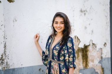 bir sokakta yıpranmış bir duvara portre genç bir uzun boylu, zarif ve güzel Hint Asyalı kadın akan içinde elbise 