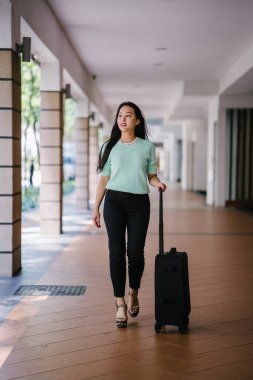 Genç bir Asyalı kadın bavulunu çekiyor. O çekici, zarif ve şık giyinmiş
