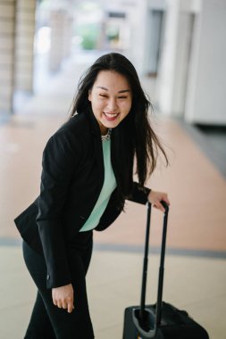 Genç bir Asyalı kadın bavulunu çekiyor. O çekici, zarif ve şık giyinmiş