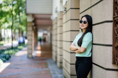 Gün boyunca bir taş duvara yaslanmış genç, seksi ve göz alıcı Asyalı bir kadının portresi. Siyah pantolonuna uyacak nane yeşili bir kazak giyiyor.