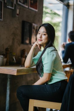 Genç ve çekici Çinli Asyalı bir kadının portresi uzanarak ve bir hafta sonu gün boyunca bir kafede rahatlatıcı. Nane yeşili bir kazak giyiyor.