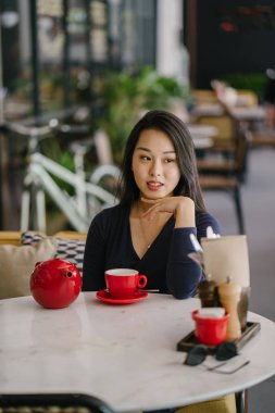 Bir açık havada açık havada oturan ve kırmızı bir çay seti çay sıcak bir fincan zevk genç, çekici, zarif ve güzel Asyalı kadın Portresi. 