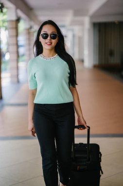 Genç bir Asyalı kadın bavulunu çekiyor. O çekici, zarif ve şık giyinmiş