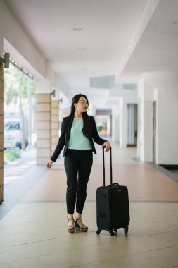 Genç bir Asyalı kadın bavulunu çekiyor. O çekici, zarif ve şık giyinmiş