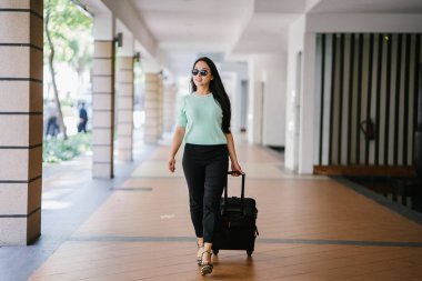 Genç bir Asyalı kadın bavulunu çekiyor. O çekici, zarif ve şık giyinmiş