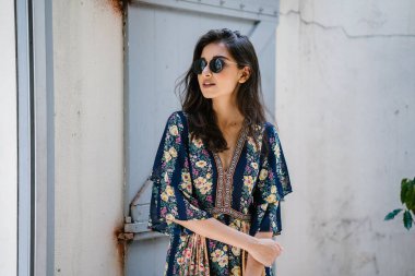 uzun boylu, zarif ve güzel Hint Asyalı kadın yaz elbise ve güneş gözlüğü gülümsüyor o pozlar gün boyunca bir arka sokakta bir sokakta olarak içinde