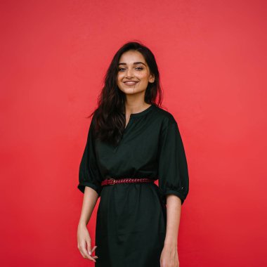 Stüdyo bir güzel, Genç ve çekici Hint Asyalı kadın kırmızı studio çerçevede bir portresi. O zarif bir basit yeşil elbise ve kırmızı kuşak giymiş ve gülüyor.
