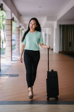 Genç bir Asyalı kadın bavulunu çekiyor. O çekici, zarif ve şık giyinmiş