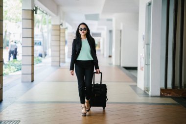 Genç bir Asyalı kadın bavulunu çekiyor. O çekici, zarif ve şık giyinmiş