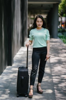 Genç bir Asyalı kadın bavulunu çekiyor. O çekici, zarif ve şık giyinmiş