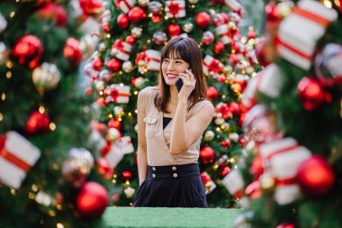 güzel orta yaşlı kadın mutlu onun smartphone üzerinde konuşuyor ve aynı derecede o durgunluk ortasında güzel gülümseyen gün boyunca Noel ağaçları dekore edilmiş olan