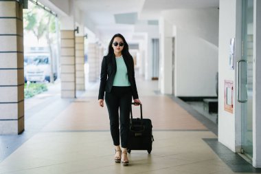 Genç bir Asyalı kadın bavulunu çekiyor. O çekici, zarif ve şık giyinmiş