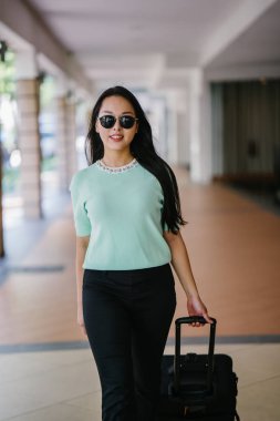 Genç bir Asyalı kadın bavulunu çekiyor. O çekici, zarif ve şık giyinmiş