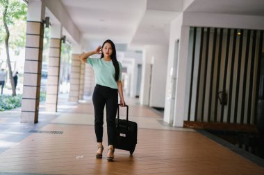 Genç bir Asyalı kadın bavulunu çekiyor. O çekici, zarif ve şık giyinmiş