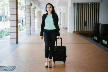 Genç bir Asyalı kadın bavulunu çekiyor. O çekici, zarif ve şık giyinmiş