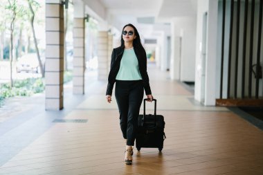 Genç bir Asyalı kadın bavulunu çekiyor. O çekici, zarif ve şık giyinmiş