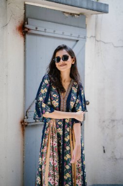 uzun boylu, zarif ve güzel Hint Asyalı kadın yaz elbise ve güneş gözlüğü gülümsüyor o pozlar gün boyunca bir arka sokakta bir sokakta olarak içinde