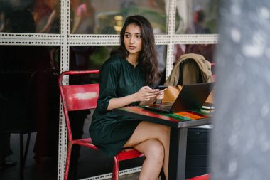 Genç Singpaorean Kızılderili kadın eğitim ya da bir kafede gün boyunca onu laptop çalışan bir mola alır gibi onun smartphone kontrol