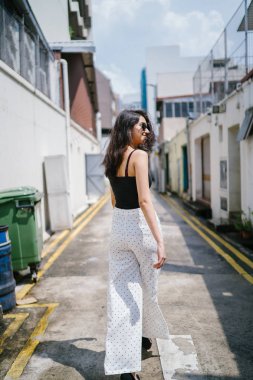 Genç, uzun boylu, ince ve zarif Hint Asyalı kadın rahat bir kıyafet içinde Asya bir sokakta bir sokakta aşağı gün boyunca yürür