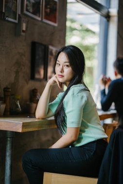 Genç ve çekici Çinli Asyalı bir kadının portresi uzanarak ve bir hafta sonu gün boyunca bir kafede rahatlatıcı. Nane yeşili bir kazak giyiyor.