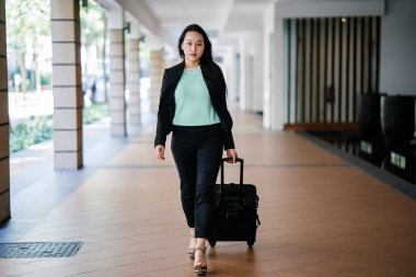 Genç bir Asyalı kadın bavulunu çekiyor. O çekici, zarif ve şık giyinmiş