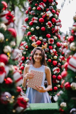 Genç, güzel ve mutlu bir Hint Asyalı kadın şenlikli Noel portresi bir hediye bir Noel ağacı önünde tutan gülümseyerek.