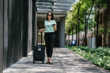 Genç bir Asyalı kadın bavulunu çekiyor. O çekici, zarif ve şık giyinmiş