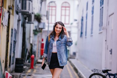 Bir genç ve çekici Hint Asyalı kadın bir kot ceket ve sarı sırt çantası onun kulaklıklar üzerinde müzik keyfi portresi