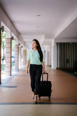 Genç bir Asyalı kadın bavulunu çekiyor. O çekici, zarif ve şık giyinmiş