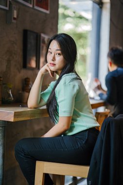 Genç ve çekici Çinli Asyalı bir kadının portresi uzanarak ve bir hafta sonu gün boyunca bir kafede rahatlatıcı. Nane yeşili bir kazak giyiyor.