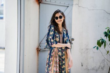 uzun boylu, zarif ve güzel Hint Asyalı kadın yaz elbise ve güneş gözlüğü gülümsüyor o pozlar gün boyunca bir arka sokakta bir sokakta olarak içinde