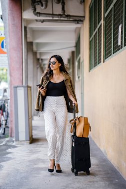 Genç ve çekici Asyalı Hint kadın arabayla aracılığıyla onun yolculuğu app onun akıllı yağıyor kitaplar. O bir geçit kendi bavullarla duruyor ve şık iş giysisi ve tonları giymiş