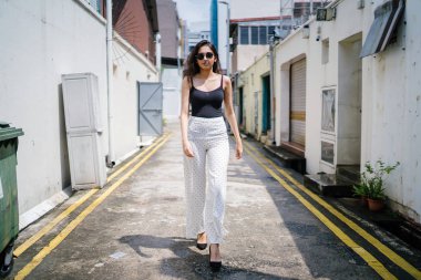 Genç, uzun boylu, ince ve zarif Hint Asyalı kadın rahat bir kıyafet içinde Asya bir sokakta bir sokakta aşağı gün boyunca yürür