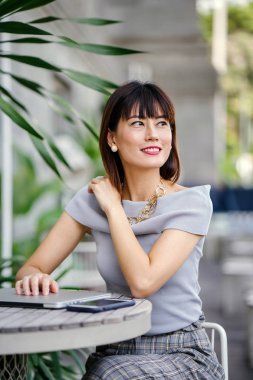 Açık havada şık bir yerde oturan bir emin, şık ve çekici orta yaşlı Çinli Asyalı kadın portresi. O bir pohpohlama gri kıyafeti giyiyor.